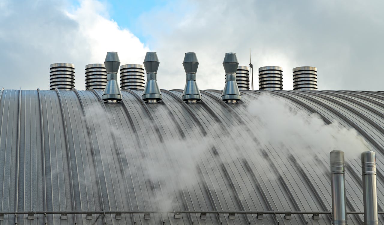 our-services-01 Photo of industrial rooftop with metal vents and steam against a cloudy sky.